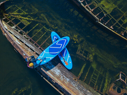 Russia, Murmansk Oblast, Kolsky District, Teriberka, Couple of sup surfers sitting on shipwreck on Barents Sea, aerial view
