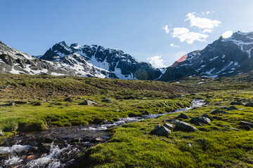 Stream flowing from melting snow near mountains against sky on sunny day