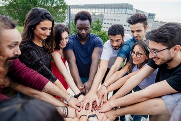 Playful male and female friends stacking hands while standing in park
