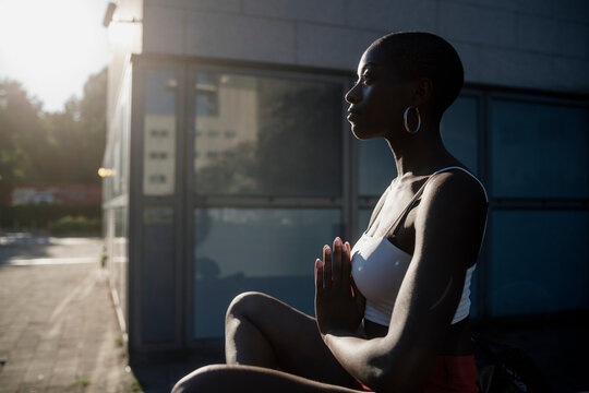 Young woman meditating while sitting outdoors in city during sunny day