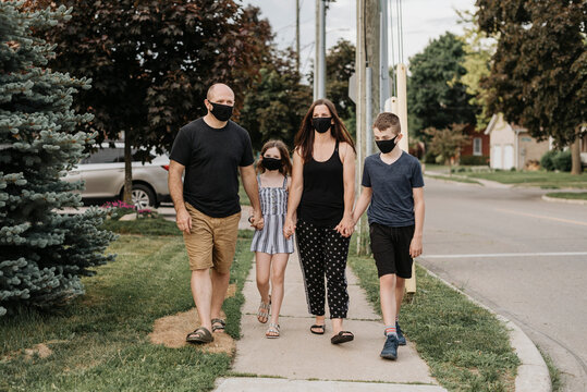 Family wearing masks holding hands while walking on footpath in city
