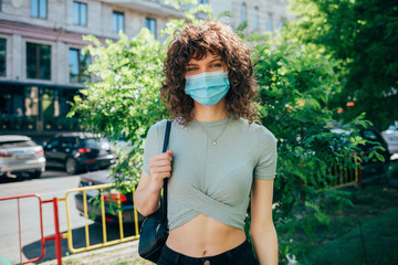 Brunette curly woman wearing protective mask in city