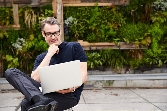 Mature man using laptop while sitting on chair at yard