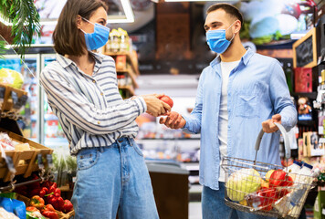 Young couple in face masks shopping in supermarket
