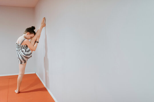 Girl stretching legs by white wall at home