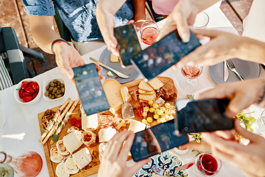 Friends having dinner with a cheese platter taking smartphone pictures