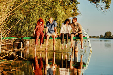 Friends reflected in water sitting on jetty at a lake
