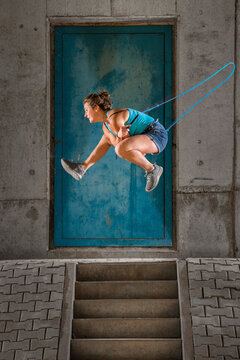 Young woman jumping over skipping rope against concrete wall under bridge