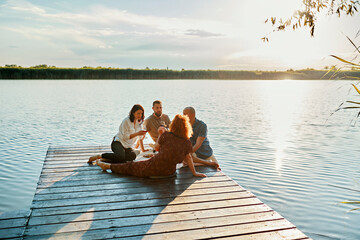 Friends having picnic on jetty at a lake at sunset