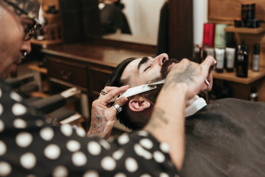 Trendy barber cutting man's beard at salon