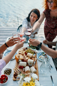 Friends having dinner at a lake clinking wine glasses