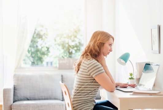Side-view of young woman working on laptop at home