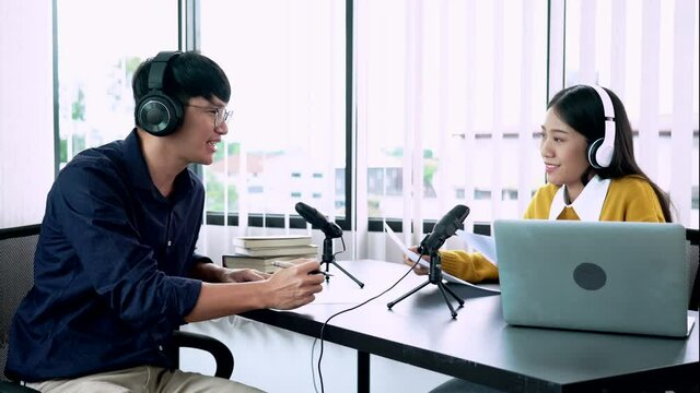 Asian woman radio hosts gesturing to microphone while interviewing a man guest in radio station during a show for radio live in the Studio
