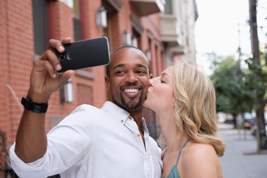 Woman kissing boyfriend in cheek, man taking selfie