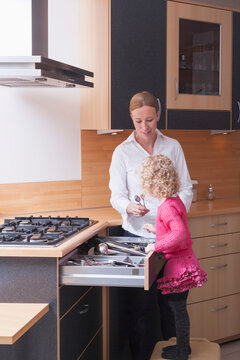 Mother helping daughter (4-5) sort kitchen utensils in drawer