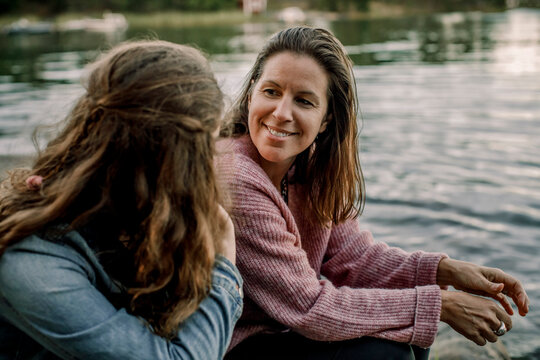 Smiling mother talking to daughter while sitting by lake