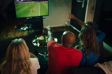 High angle view of friends watching sports on TV while sitting on sofa in living room