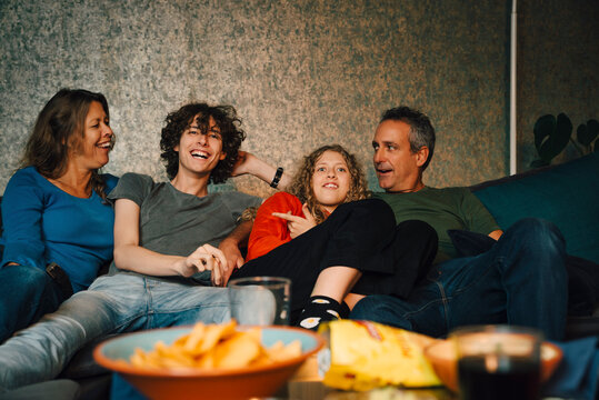 Smiling parents with children watching sports in living room at night