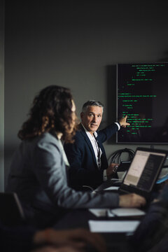 Businessman pointing at projection screen while discussing with coworker at workplace