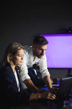 Male professional working on laptop by female colleague at workplace