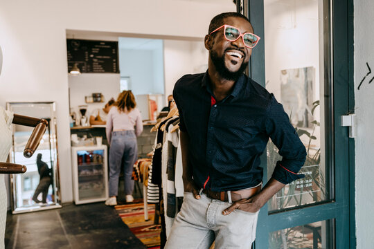 Smiling owner with hands in pockets standing at doorway of clothing store