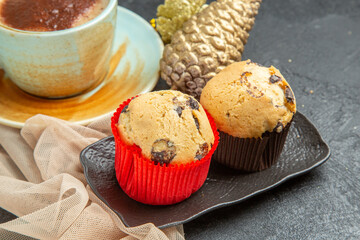 Close up view of a cup of frothy coffee on towel with accessory and small cupcakes on dark background