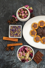 half left view of a plate of cookies with dry flowers and cinnamons and chocolates on grey ground