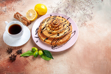 Obraz na płótnie Canvas Side view of classic pancakes and a cup of tea fruits cinnamon on colourful table