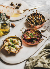 Various Mediterranean vegetarian meze in copper dishes, olive oil and fresh bread over marble table background, selective focus. Aegean cuisine concept