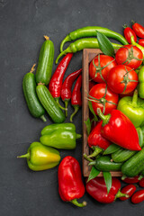 Vertical view of fresh vegetables inside and outside of a brown wooden basket on the left side on dark background