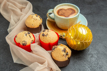 Front close view of delicious freshly baked small cupcakes and a cup of frothy coffee on towel accessory on black background