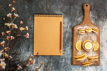 Classic American pancakes with lemons on cutting board with flowers and notebook on gray background