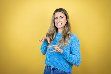 Pretty blonde woman with long hair standing over yellow background disgusted expression, displeased...