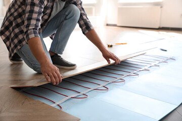 Professional contractor installing underfloor trace heating system indoors, closeup