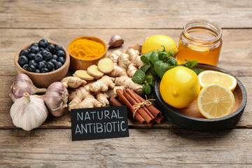 Different fresh products and card with phrase Natural Antibiotic on wooden table