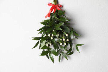 Mistletoe bunch with red bow hanging on white wall. Traditional Christmas decor