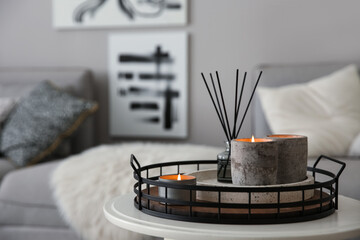 Candles and aroma reed diffuser on white table near grey sofa, space for text - obrazy, fototapety, plakaty