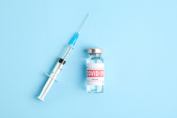 Vial with coronavirus vaccine and syringe on light blue background, flat lay