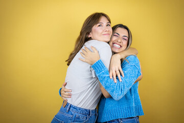 Two pretty women standing over yellow background having fun