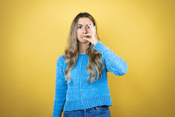 Pretty blonde woman with long hair standing over yellow background with mouth and lips shut as zip...