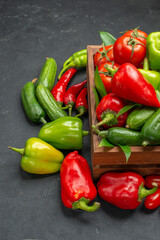 Vertical view of fresh vegetables inside and outside of a brown wooden basket on the left side on dark table