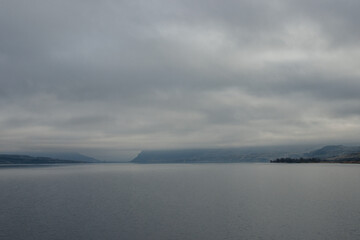 A beautiful foggy landscape in a blue-gray scale: a wide river, in front of the horizon are dark blue mountains, on the banks of the hills with dry grass. Colorado river, OR, USA