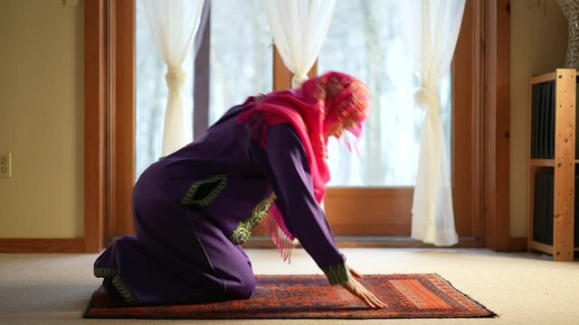 Mature Muslim woman praying at home with beautiful light with snow on the ground. Concept of female prayer in home environment.