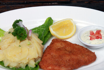 Bread crumbed fish fillet served with potato salad, sauce tartar and lime
