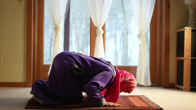 Mature Muslim woman praying at home with beautiful light with snow on the ground. Concept of female prayer in home environment.
