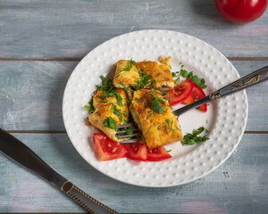Breakfast with omelet and tomatoes sprinkled with herbs on a round white plate with a fork