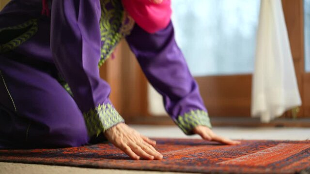 Mature Muslim woman praying at home with beautiful light with snow on the ground. Concept of female prayer in home environment.