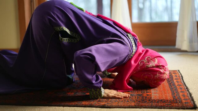 Mature Muslim woman praying at home with beautiful light with snow on the ground. Concept of female prayer in home environment.