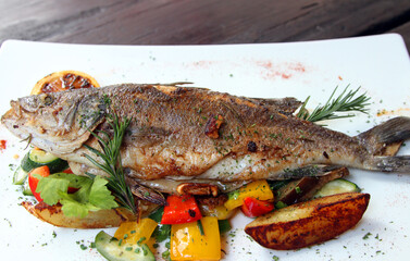 Grilled sea bass on Mediterranean vegetables, grilled lemon slice  and potato wedges