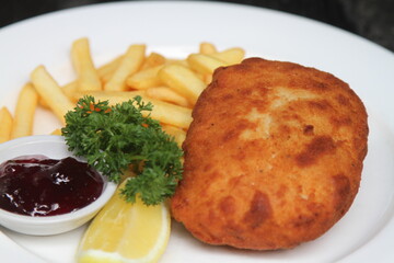 Filled pork schnitzel called Cordon Bleu with French fries, cranberry jam and lemon